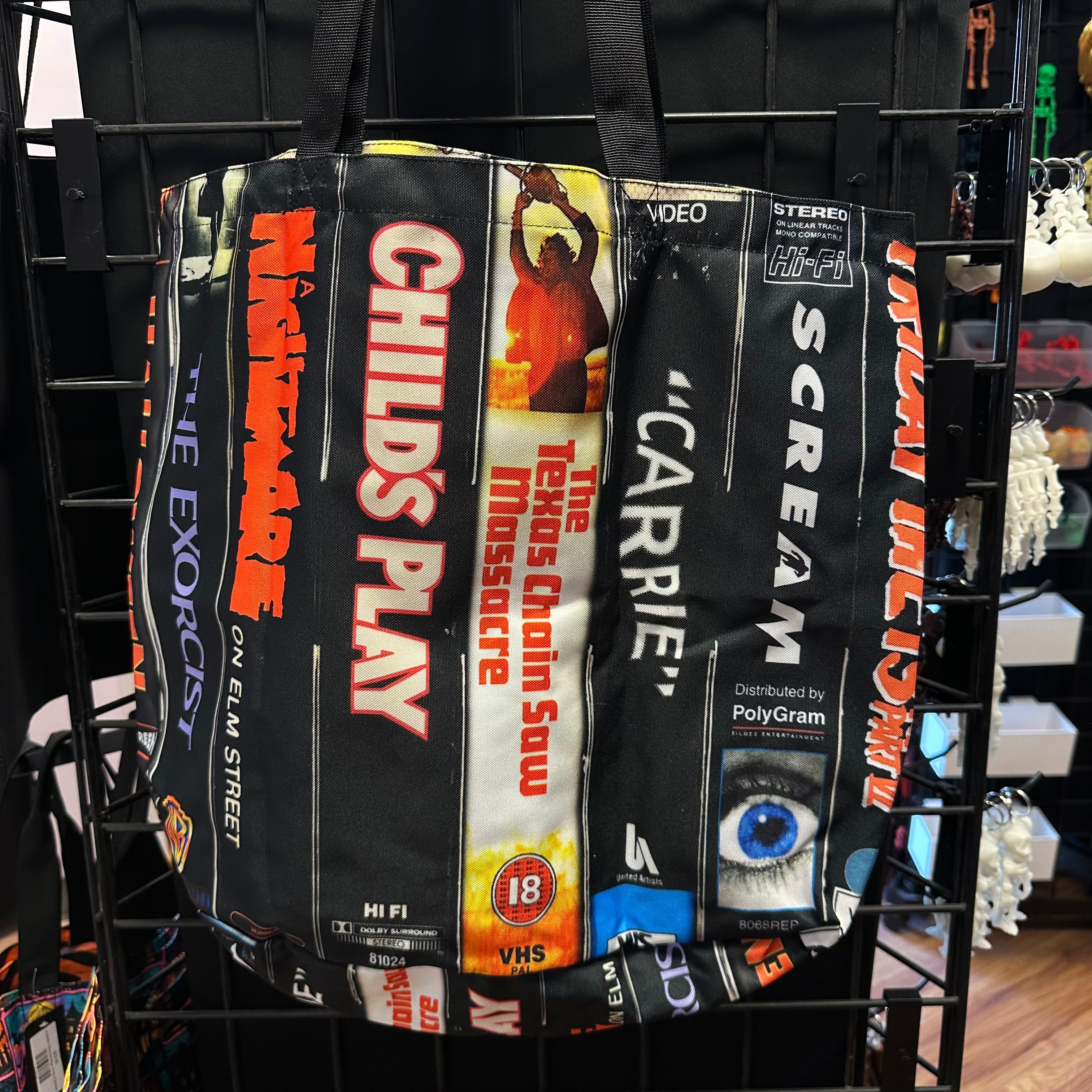 A black tote bag featuring VHS-style movie cover prints hanging on a black display rack.